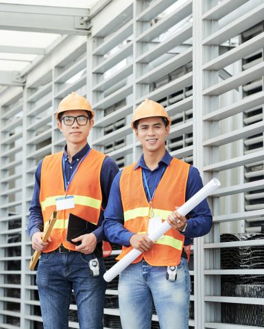 Young Asian heavy industry engineers with blueprint and construction level